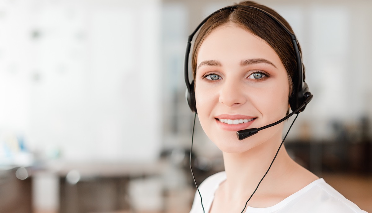 Smiling young office worker with a headset  answering in a call center, woman talking with clients. Portrait of an attractive customer and technical support representative. Business concept